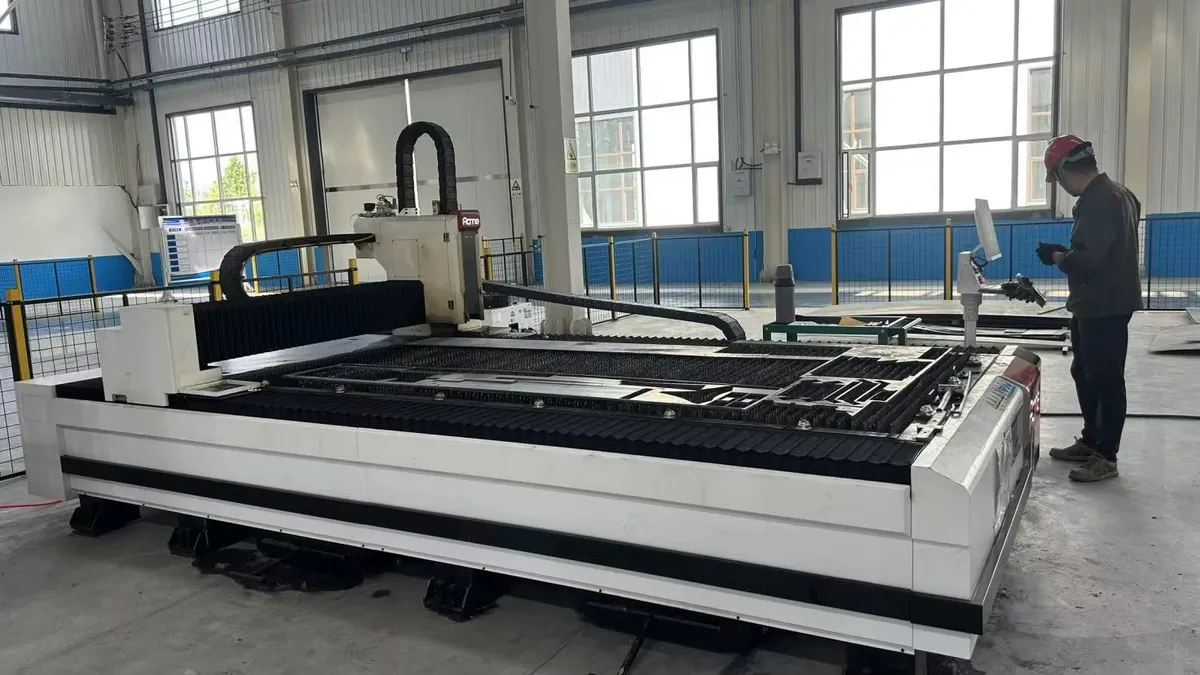 Worker in a hard hat operates a large industrial laser cutting machine in a factory.